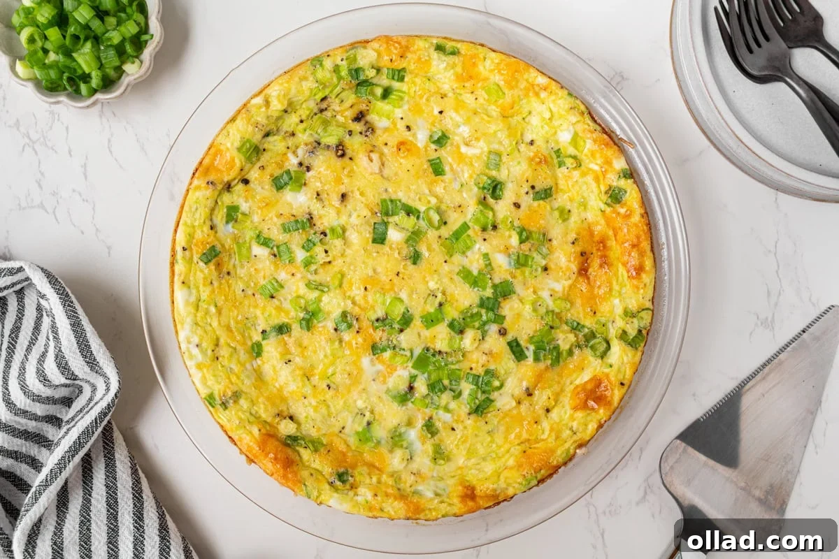 An inviting overhead shot of a perfectly baked crustless zucchini quiche, boasting a beautiful golden-brown top and delicately sprinkled with fresh green onions, sitting in its pie dish, inviting a first slice.