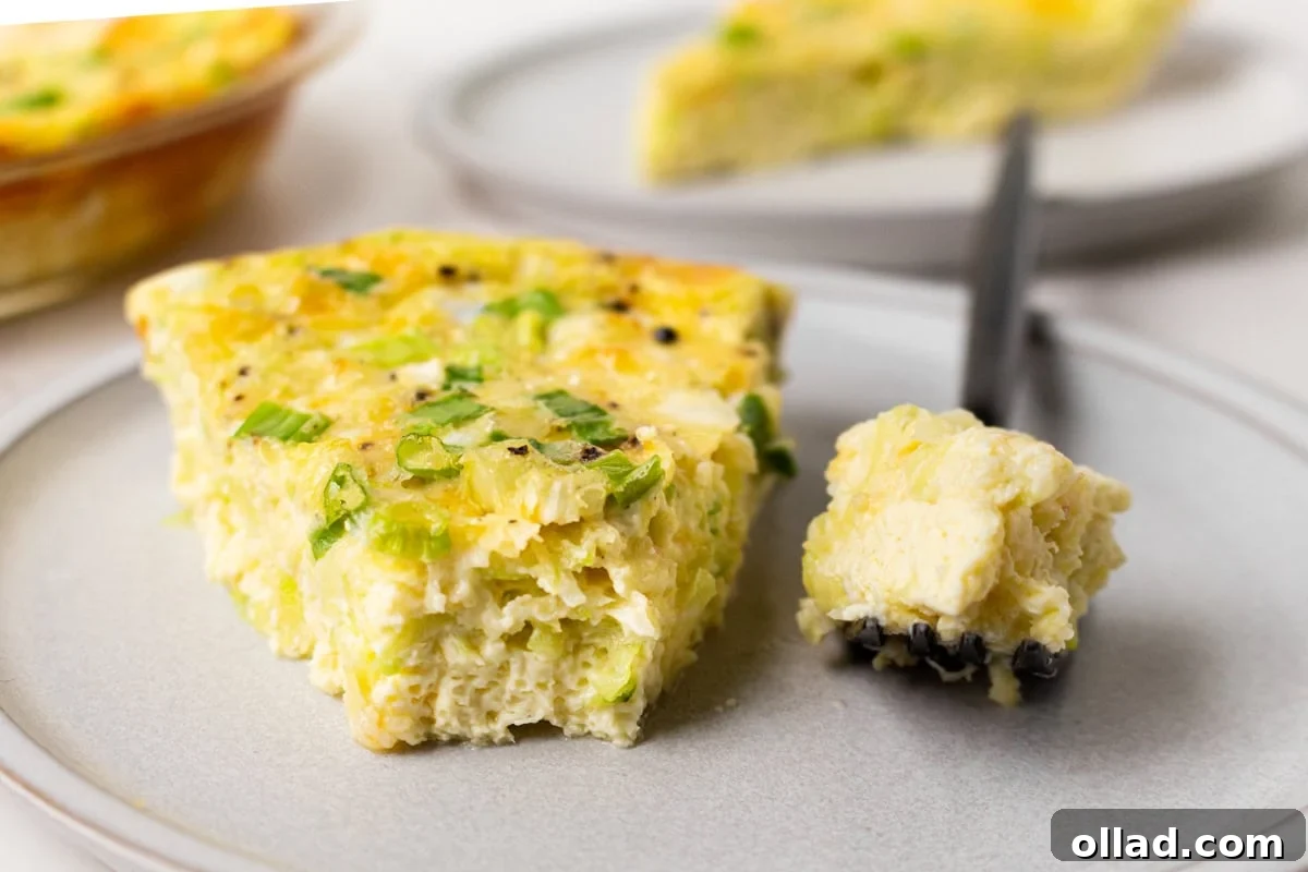 A close-up of a delectable slice of crustless zucchini quiche on a pristine white plate, with a fork poised to capture a bite, revealing the fluffy, cheesy, and vegetable-rich interior.