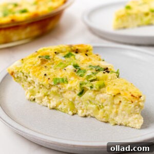 A slice of crustless zucchini quiche on a gray plate, topped with green onions, with the full quiche visible in the background.