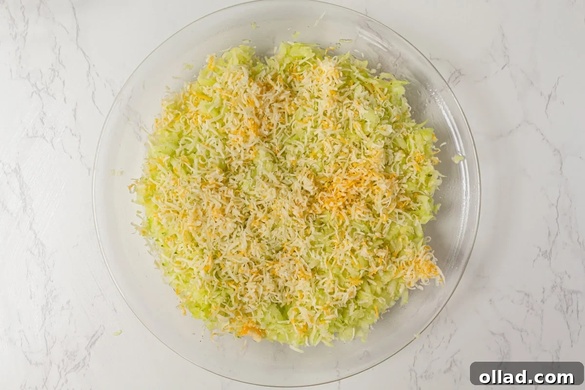 A delightful layering of finely shredded zucchini, followed by a generous layer of mixed Colby Jack and Gruyere cheese, elegantly arranged within a pie plate, forming the delicious base of the quiche.