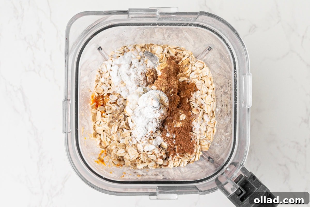 Rolled oats, baking powder, cinnamon, pumpkin spice, and ginger added to the wet pumpkin mixture in the blender.