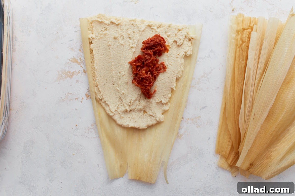 A softened corn husk with masa dough spread over it and a spoonful of pork filling in the center.