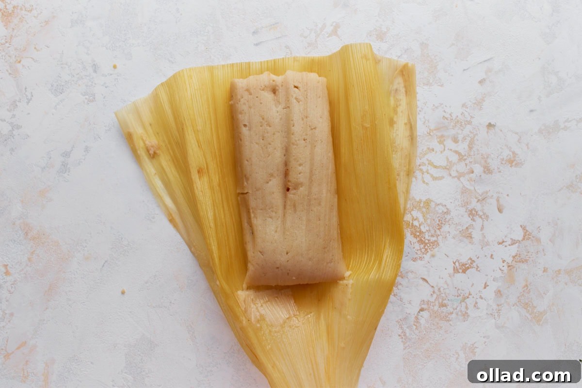 A single cooked tamale unwrapped from the corn husk, showing its soft, smooth masa texture.