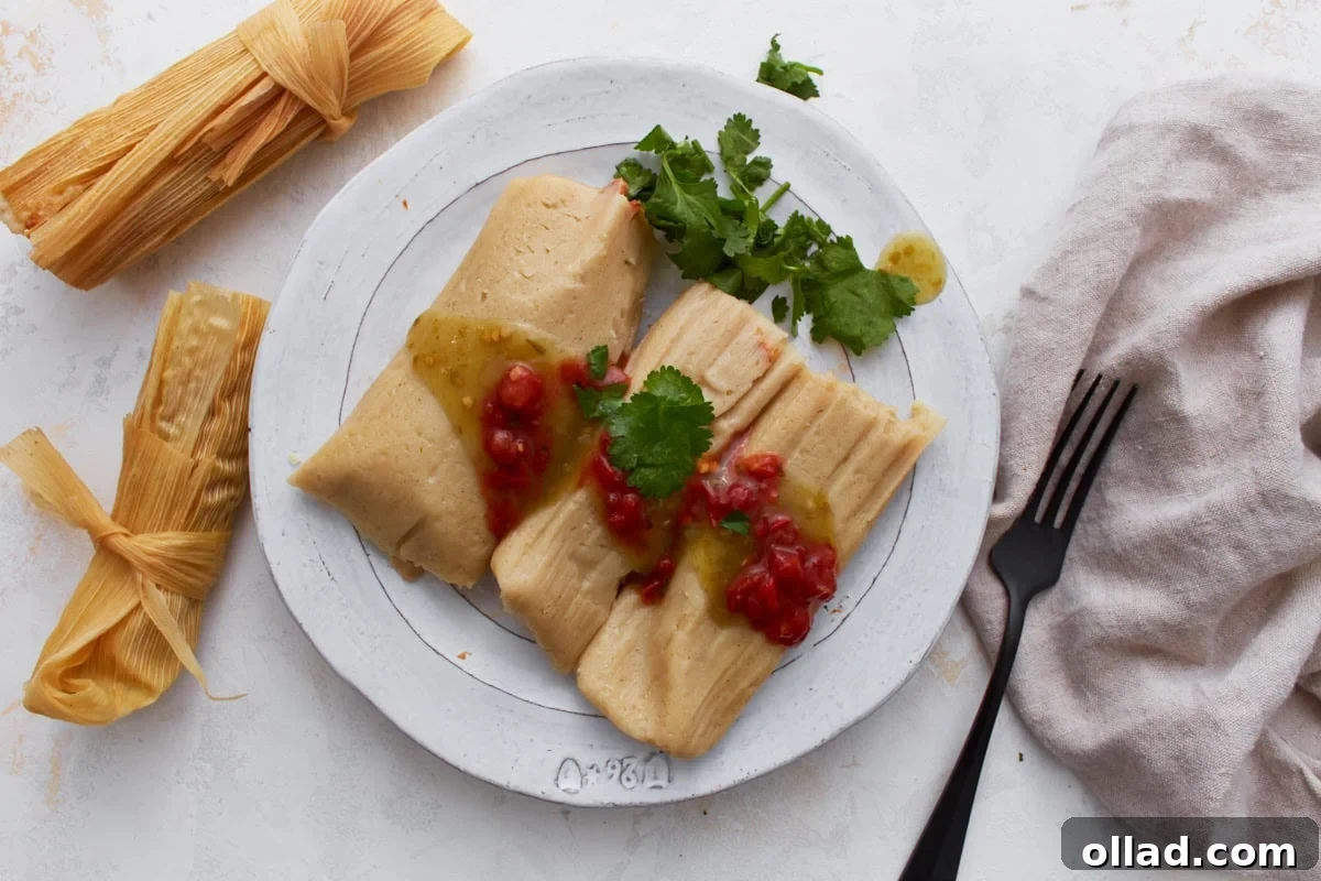 Two gluten-free tamales served on a white plate topped with green salsa and red sauce, garnished with fresh cilantro.