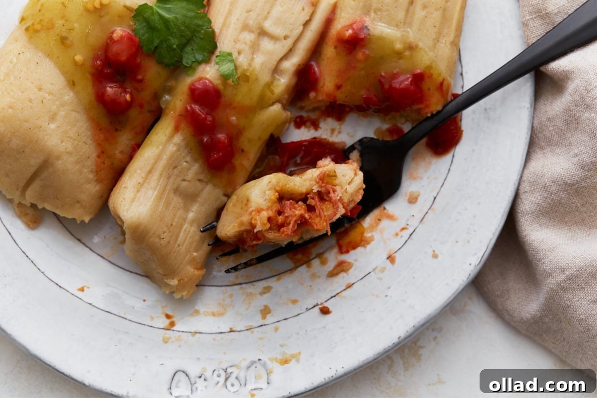 Close-up of a tamale cut open on a fork, showing the red pork filling inside.