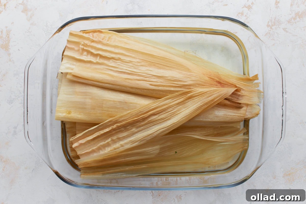 Dried corn husks soaking in hot water inside a glass baking dish until pliable.