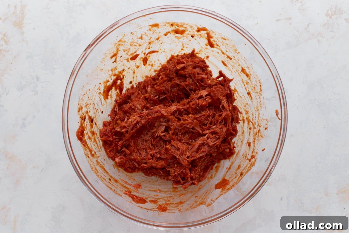 Shredded pork mixed with red enchilada sauce in a glass bowl.
