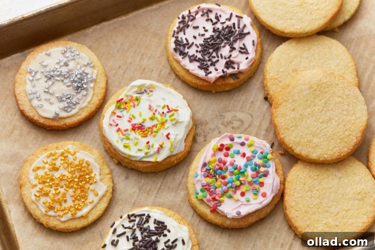 Almond flour sugar cookies decorated with colorful frosting and sprinkles next to plain baked cookies on a parchment-lined sheet.