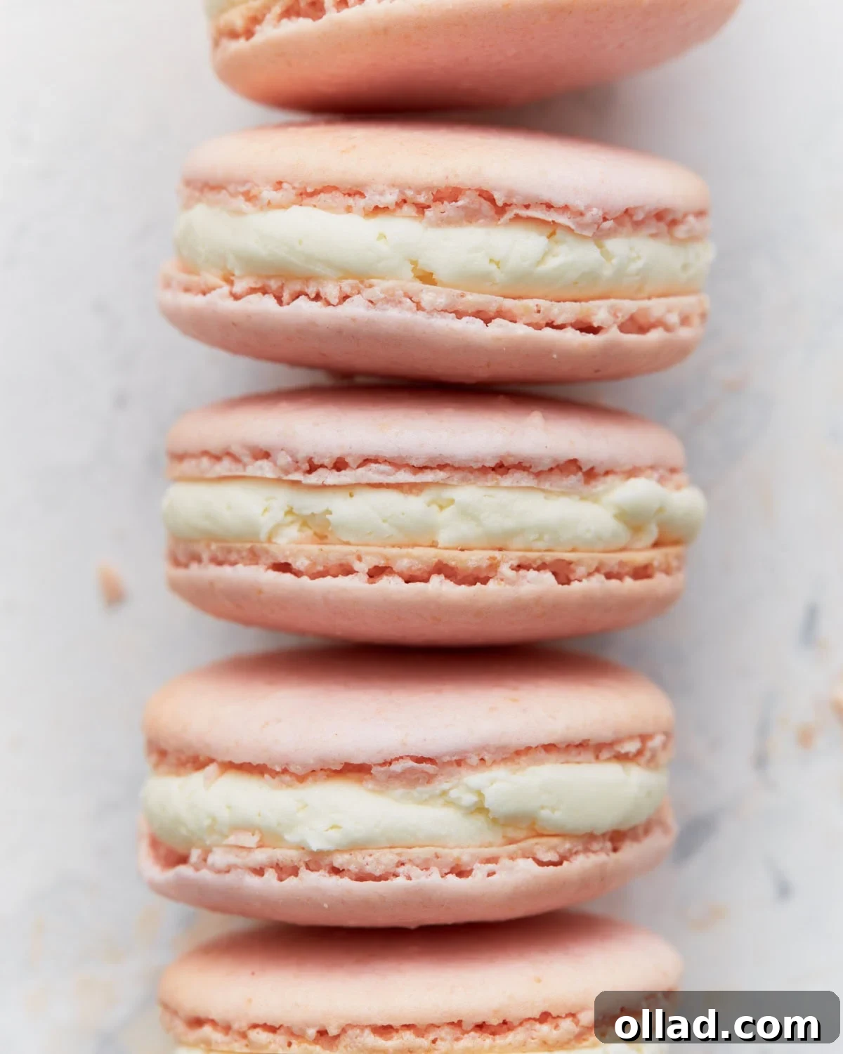 Irresistible Gluten-Free French Macarons 2 Close-up stack of perfectly piped pink French macarons with creamy vanilla buttercream filling, showcasing their smooth, dome-shaped tops and characteristic ruffled 'feet'.