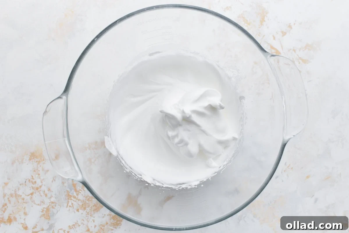 Irresistible Gluten-Free French Macarons 6 A pristine, glossy egg white meringue, whipped to stiff peaks in a clear glass mixing bowl, demonstrating the perfect consistency for macaron making.