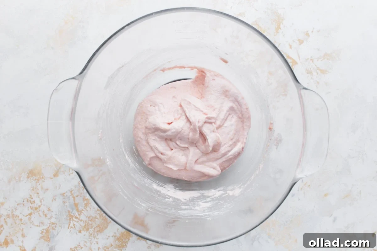 Irresistible Gluten-Free French Macarons 8 The macaron batter, now a soft pink hue, is shown after proper macaronage, exhibiting a thick, flowing ribbon consistency that indicates readiness for piping.