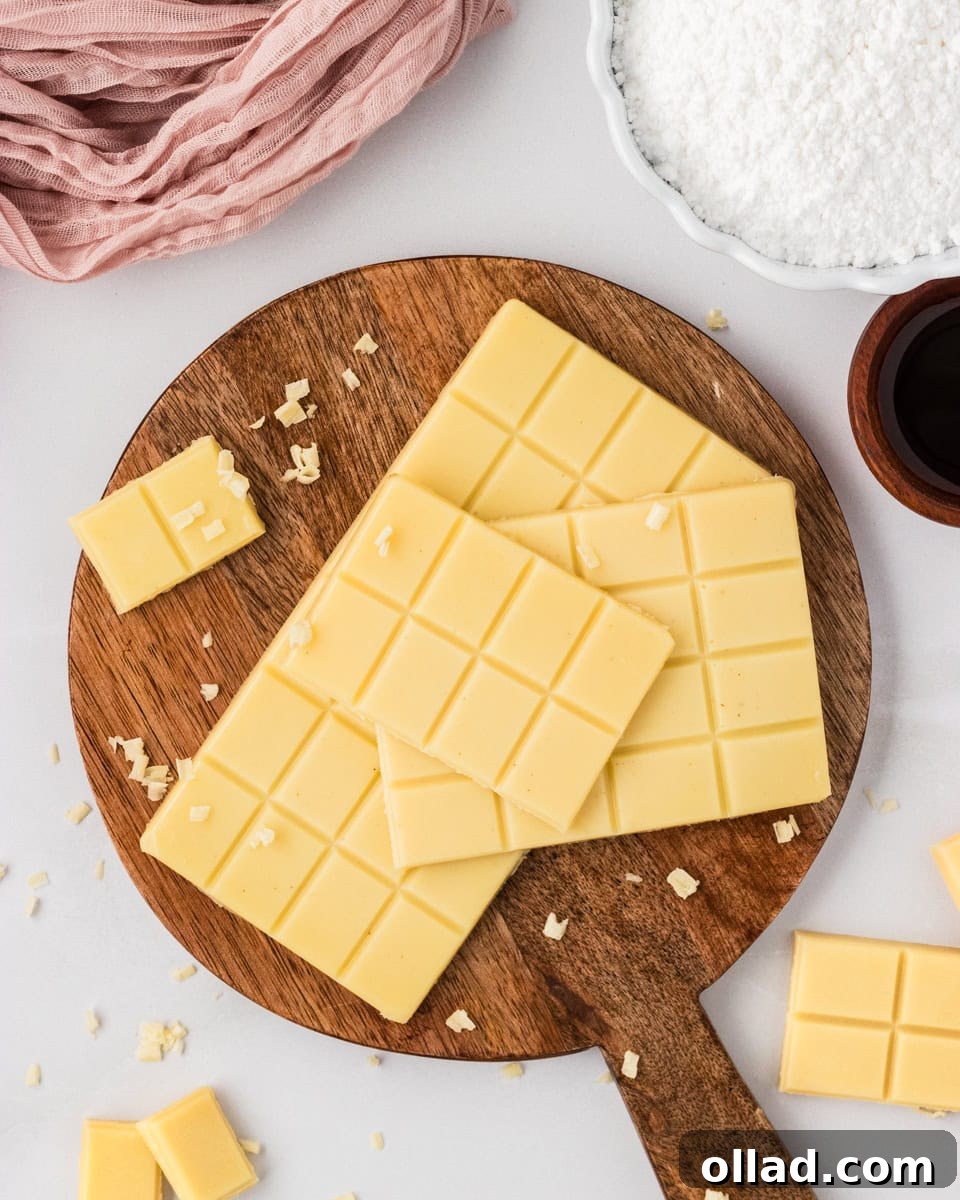Vegan white chocolate bars stacked on a wooden board with small shaved pieces scattered around.
