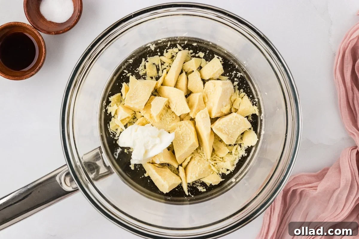 Chopped cacao butter and vegetable shortening in a glass bowl over a pot, ready to melt.