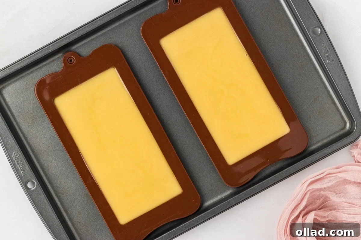Smooth chocolate mixture poured into silicone bar molds on a baking sheet.