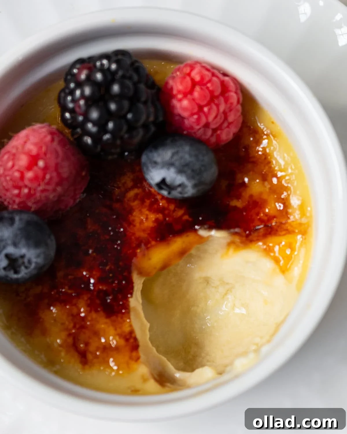 Dairy-free crème brûlée with a crackly caramelized sugar top, garnished with fresh berries in a white ramekin.