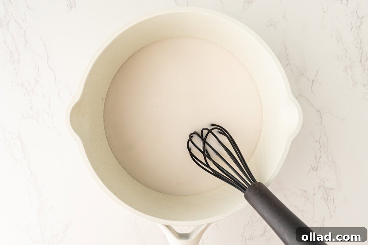 Full-fat coconut milk and sugar heating in a saucepan on the stovetop.