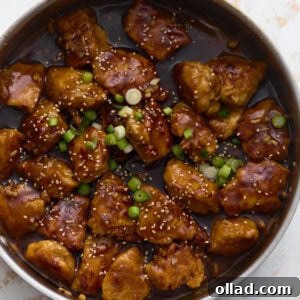 Gluten-free General Tso’s chicken coated in a glossy sweet and spicy sauce, garnished with green onions and sesame seeds in a skillet