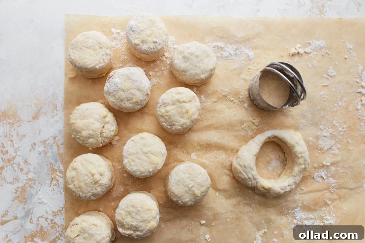 Unbaked gluten-free biscuit rounds arranged on parchment paper, with a biscuit cutter and dough scraps nearby, illustrating the cutting process.