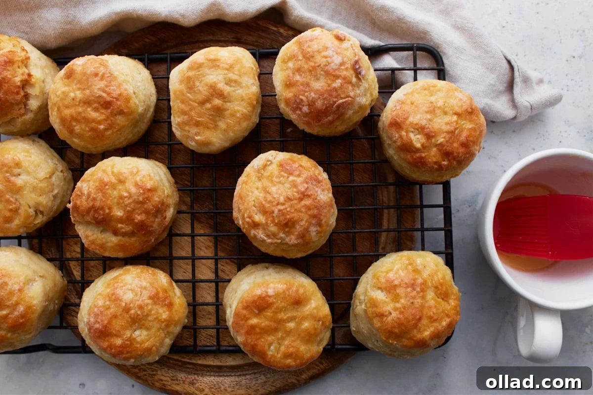 Baked biscuits cooling on a wire rack, with a pastry brush and a small cup of melted butter nearby, ready for a final buttery touch.