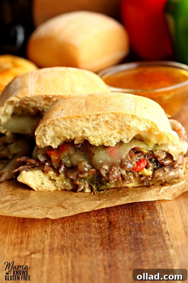 An Instant Pot steak sandwich cut in half, showcasing the tender beef and vegetables inside, with a roll and au jus in the background.