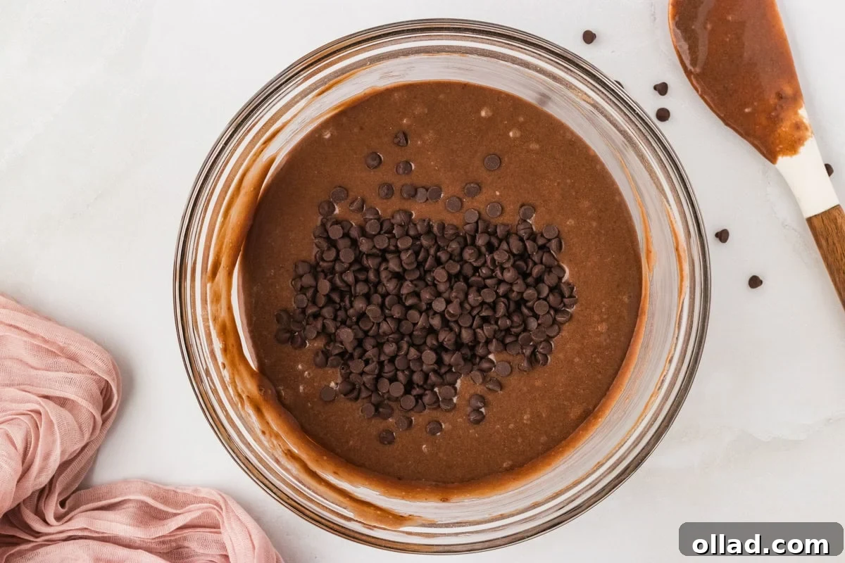Decadent Gluten-Free Double Chocolate Muffins 7 Bowl of smooth chocolate muffin batter with mini chocolate chips just added on top, poised to be gently folded in with a spatula.