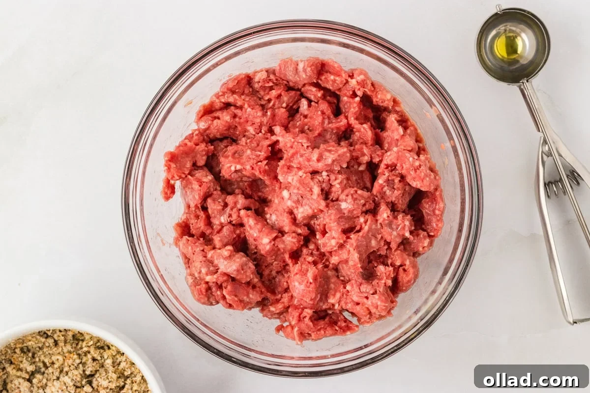 Delicious Gluten-Free Meatballs 7 Raw ground beef in a glass mixing bowl with a cookie scoop and measuring spoon beside it.