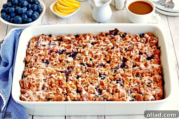 A pan of gluten-free blueberry lemon breakfast casserole, beautifully garnished, with fresh blueberries, lemon slices, creamer, and a cup of coffee blurred in the background, setting a perfect breakfast scene.