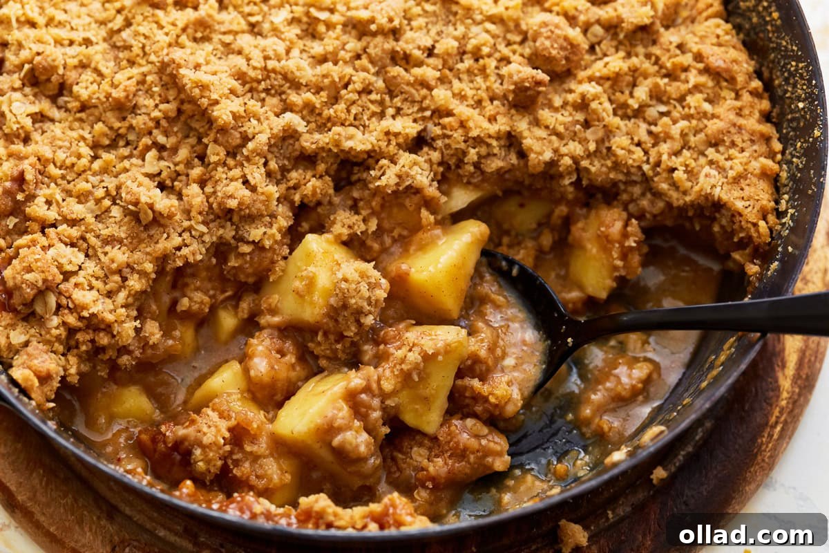 Wholesome Gluten-Free Apple Crumble 4 A serving of gluten-free apple crisp being scooped from a white baking dish into a bowl, showcasing the rich apple filling and golden oat topping.