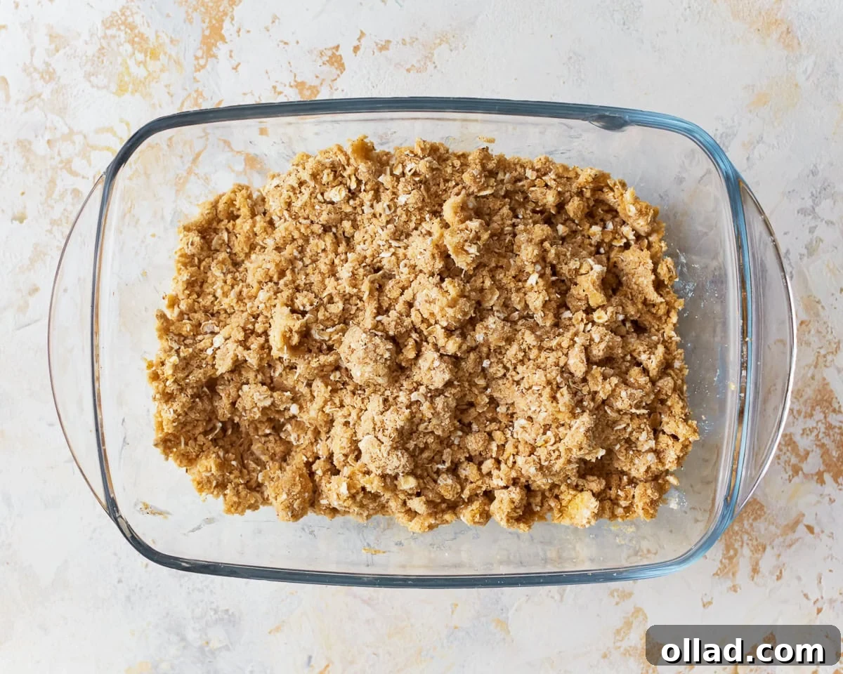 Wholesome Gluten-Free Apple Crumble 6 A glass baking dish sits on a countertop, with a bowl of chunky crumb topping for gluten-free apple crisp next to it, showing the texture of the oats and flour.