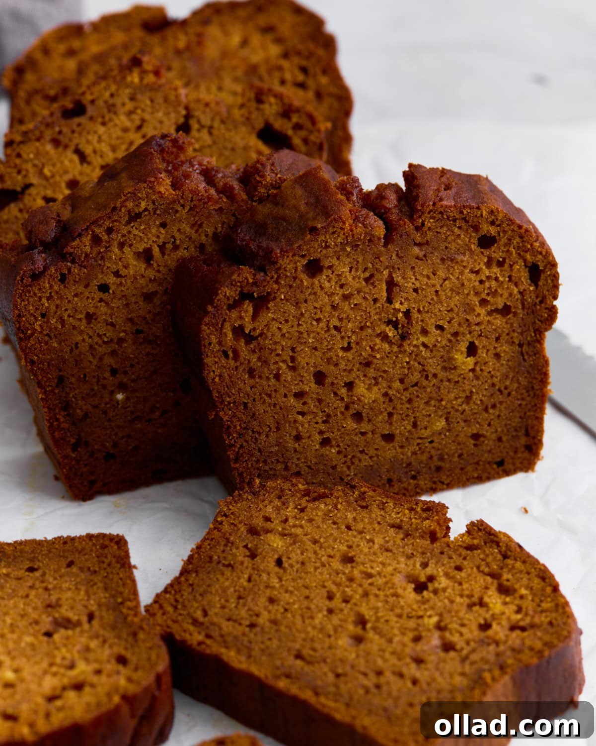 Slices of moist gluten-free pumpkin bread on parchment paper, showing a soft crumb and golden-brown crust.