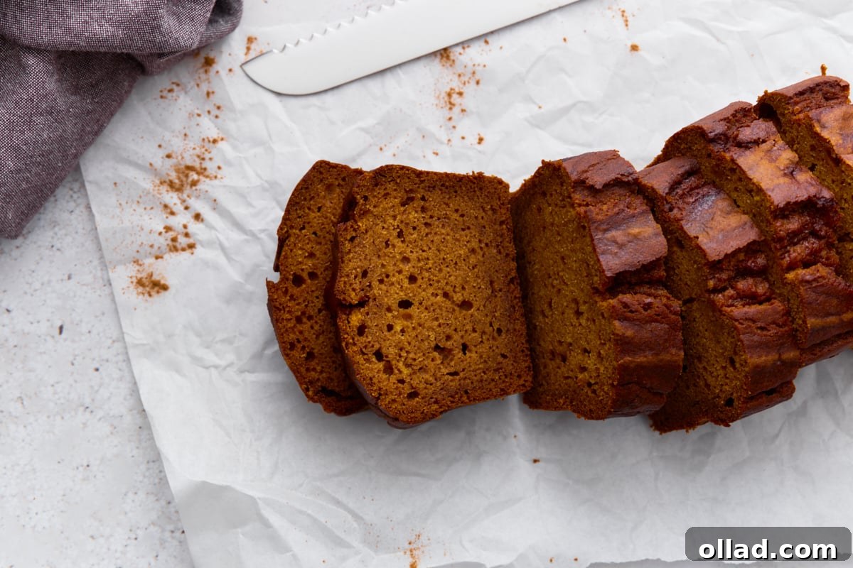 Pumpkin bread sliced on parchment paper with a serrated knife nearby, crumbs scattered.