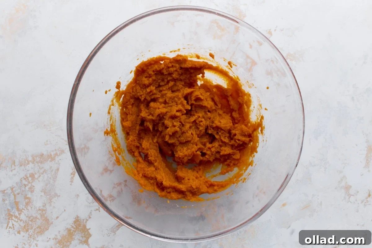 Glass mixing bowl with canned pumpkin puree partially mixed, sitting on a light counter.