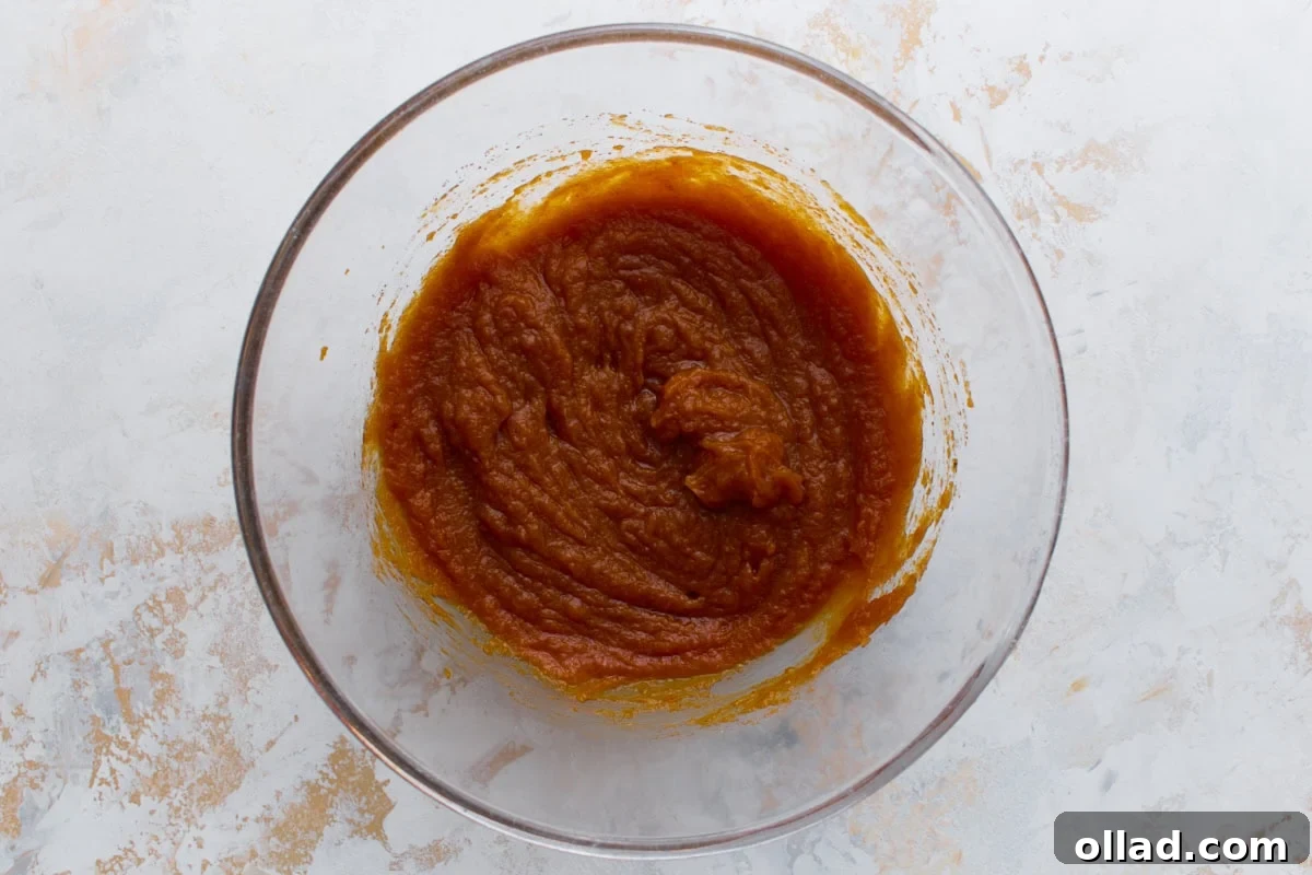 Pumpkin puree mixed with sugars and vanilla in a glass bowl, creating a smooth orange base.