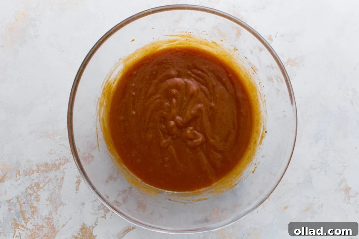 Pumpkin mixture whisked with eggs and oil in a clear bowl until glossy and smooth.