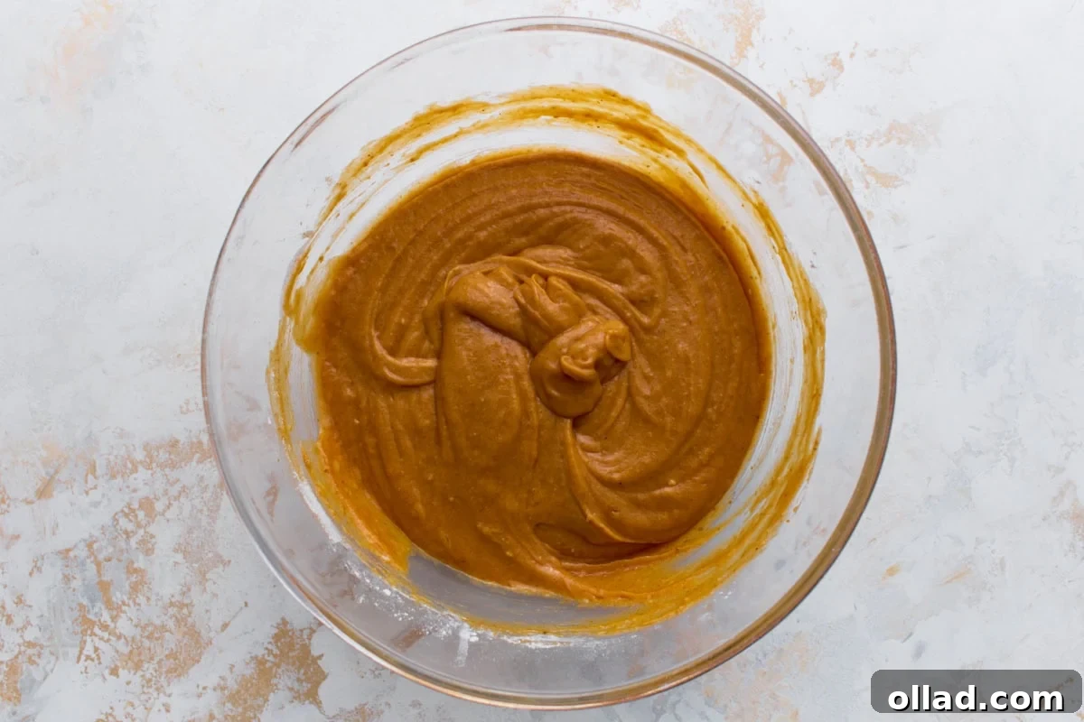 Thick pumpkin bread batter combined with flour and spices in a glass bowl.