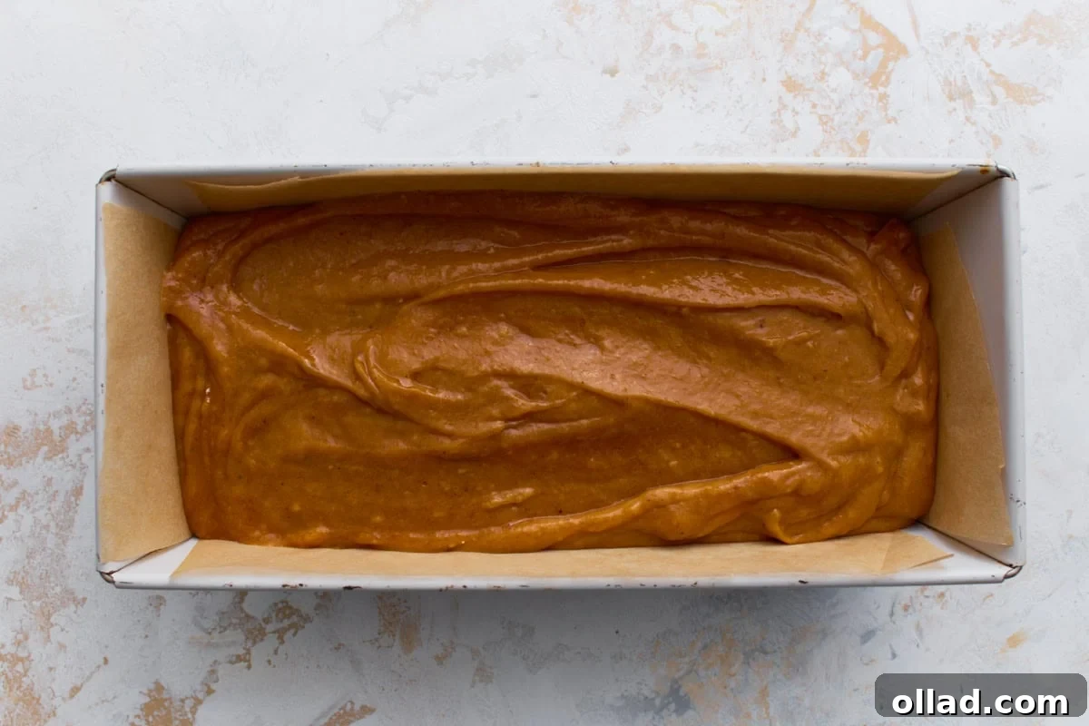 Pumpkin bread batter spread evenly into a parchment-lined loaf pan before baking.