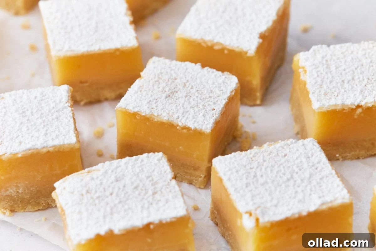 Close-up of gluten-free lemon bars, featuring a thick, vibrant yellow lemon filling on a shortbread crust, dusted generously with powdered sugar, arranged neatly on parchment paper