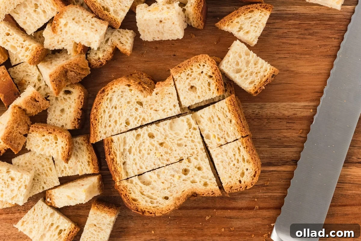 Slices of gluten-free bread cut into cubes on a wooden cutting board, next to a bread knife.