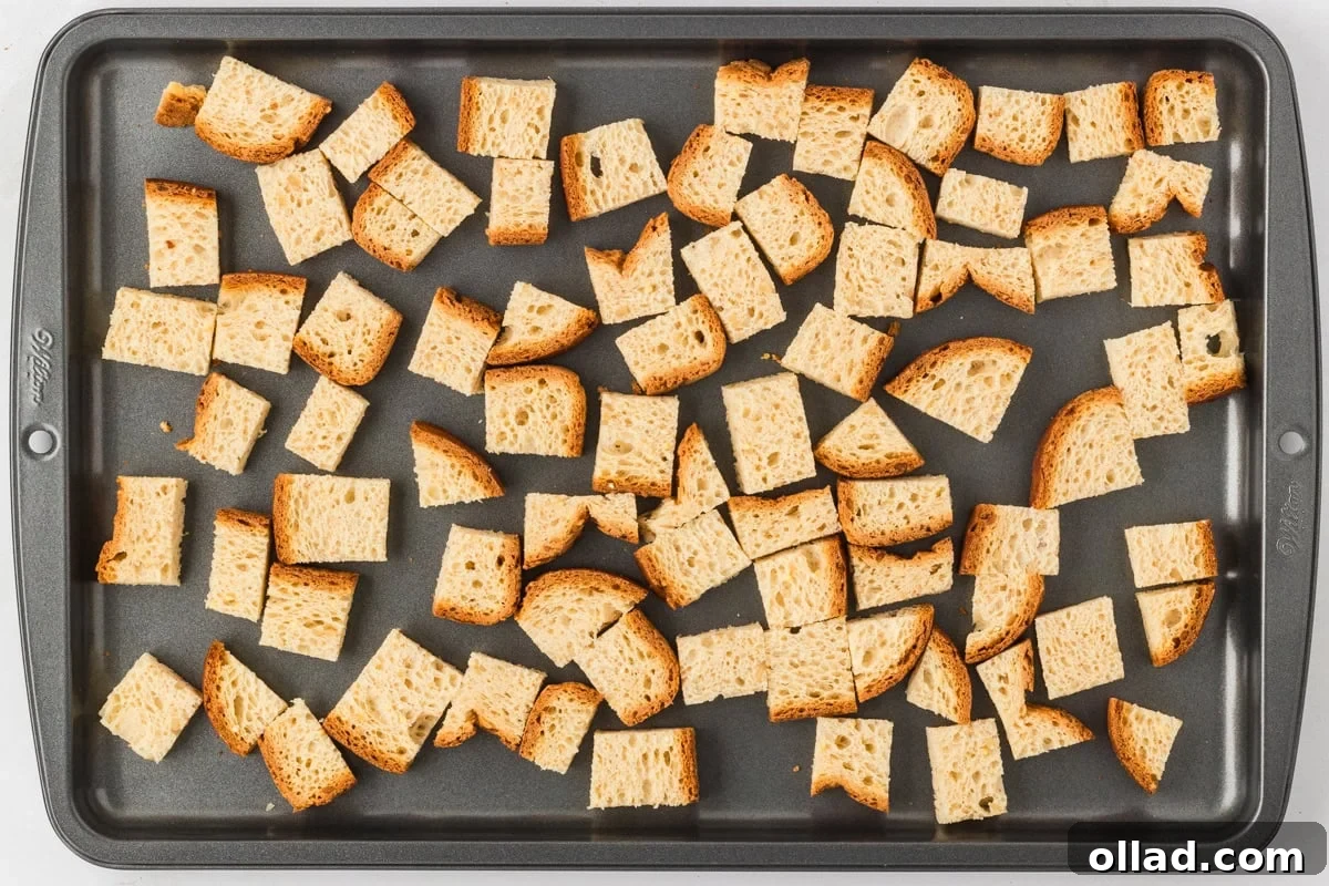 Evenly spaced cubes of gluten-free bread on a baking sheet, ready to be toasted.