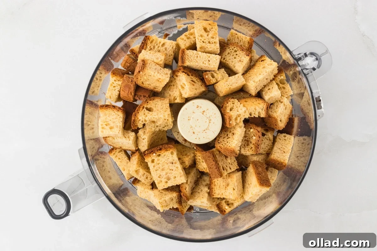 Toasted bread cubes placed inside a food processor bowl, ready to be ground into breadcrumbs.