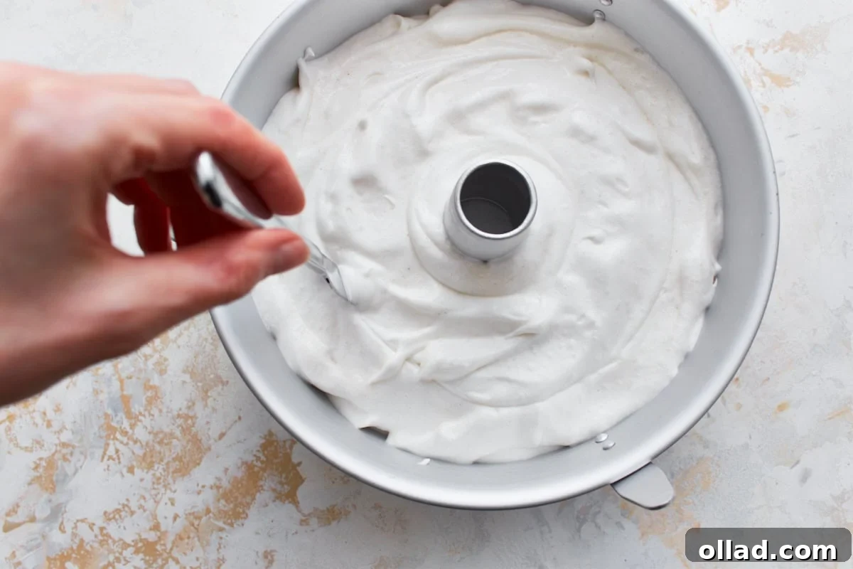 Cloud-Light Gluten-Free Angel Food Cake 10 A hand using a butter knife to gently cut through gluten-free angel food cake batter in an ungreased tube pan, releasing air bubbles.
