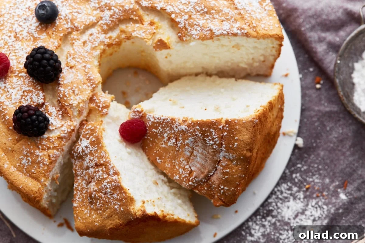 Cloud-Light Gluten-Free Angel Food Cake 15 A beautifully presented gluten-free angel food cake, with two slices artfully placed on their side, garnished with a dusting of powdered sugar and vibrant fresh berries.