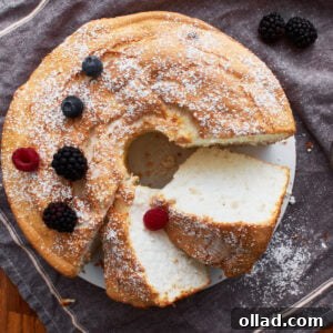 Cloud-Light Gluten-Free Angel Food Cake 3 gluten-free angel food cake sliced on a grey towel sprinkled with powdered sugar and a few berries.