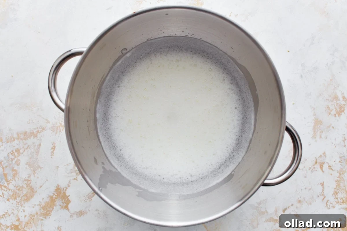 Cloud-Light Gluten-Free Angel Food Cake 6 Foamy egg whites and cream of tartar being beaten together in a shiny stainless steel mixing bowl using a stand mixer.