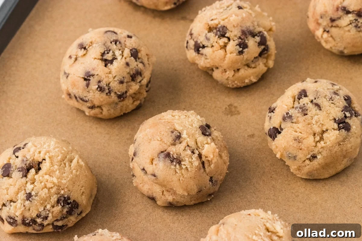 Irresistible Gluten-Free Cookie Dough 10 A close-up shot of perfectly formed gluten-free edible cookie dough balls resting on a crinkled parchment-lined baking sheet, appearing rich and inviting, ready to be enjoyed or further chilled.