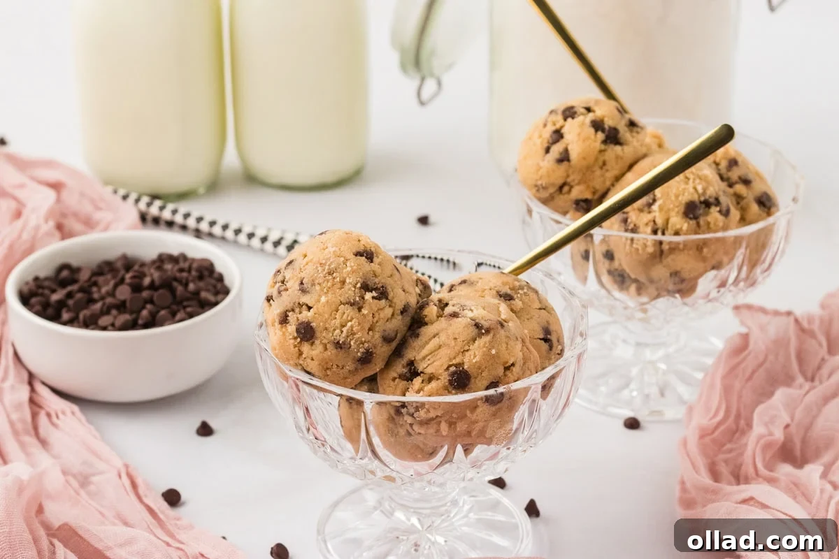 Irresistible Gluten-Free Cookie Dough 11 Elegant glass dessert cups, each generously filled with velvety scoops of gluten-free edible cookie dough. Mini chocolate chips are scattered around, while two glasses of refreshing milk stand blurred in the background, completing a tempting dessert display.