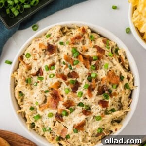 A bowl brimming with creamy Instant Pot Crack Chicken, beautifully garnished with fresh chopped green onions and delectable crispy bacon pieces. A scattering of various fresh toppings and crunchy chips surround the bowl, suggesting multiple serving possibilities.