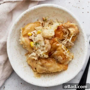 A perfect serving of gluten-free chicken and dumplings casserole on a clean white speckled plate. Visible layers include fluffy biscuit topping, tender shredded chicken, sweet corn, and a rich, creamy sauce, all ready to be savored with a fork.