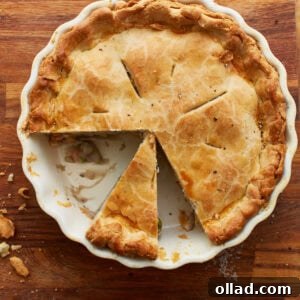 An inviting overhead view of a golden-crusted gluten-free chicken pot pie in a white pie pan on a wooden countertop. Two slices have been removed, revealing the rich, creamy filling beneath, and another slice is perfectly cut, ready to be served.