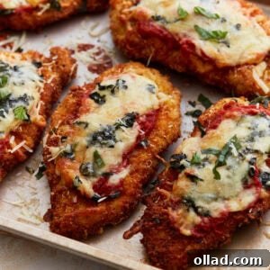 Crispy, golden-brown gluten-free chicken parmesan topped with melted cheese, marinara sauce, and fresh basil, presented beautifully on a baking sheet. The cheese is bubbly and the chicken looks perfectly cooked.